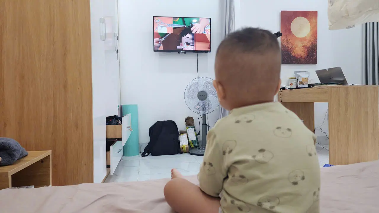 Một bé trai đang ngồi tập trung xem tivi cùng cha, ánh mắt chăm chú vào nội dung giáo dục trên màn hình.